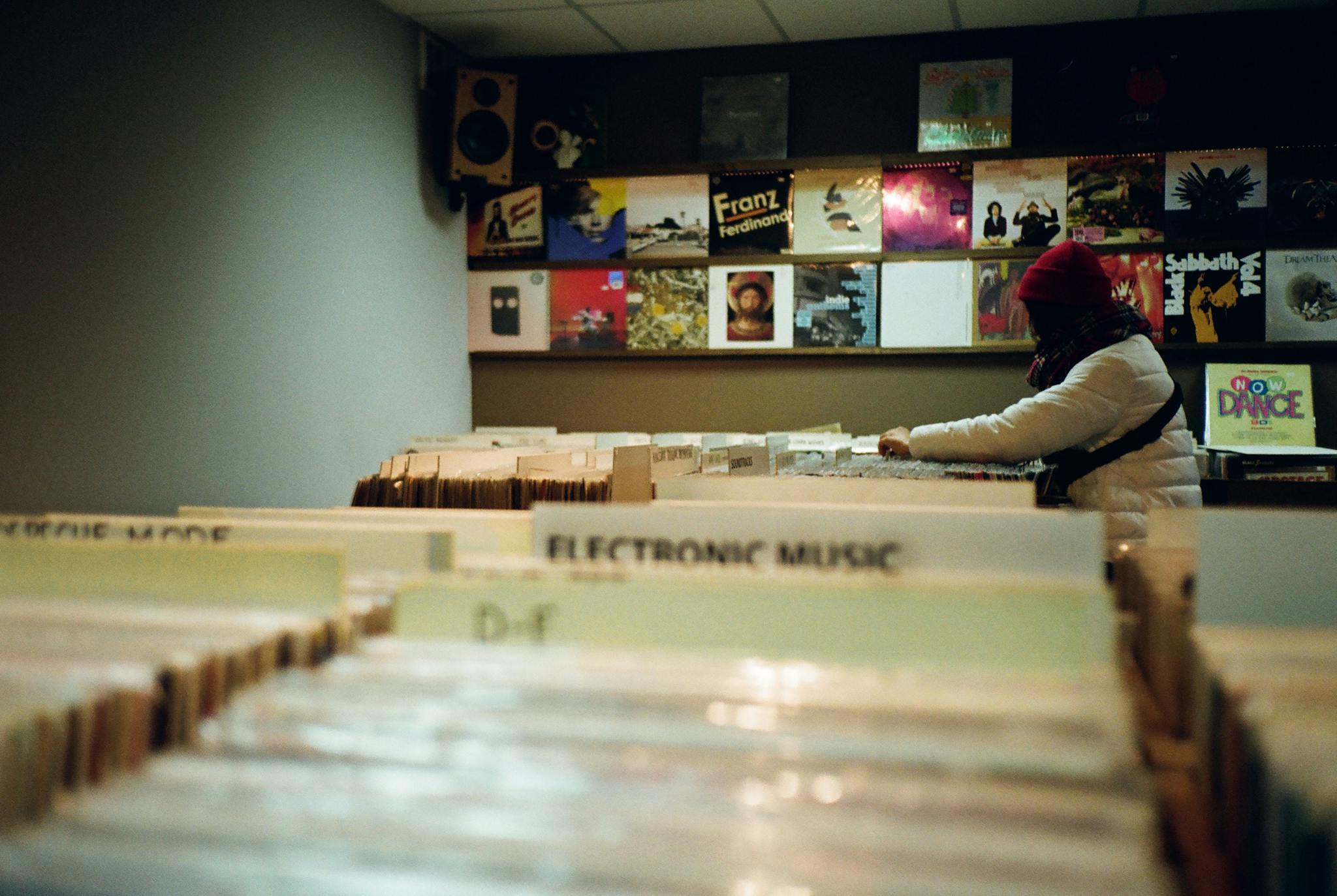 A person explores a variety of vinyl records in a cozy store, adding a nostalgic touch to the scene.