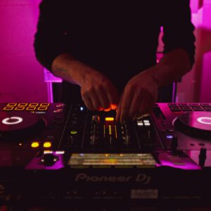 Close-up of DJ hands mixing music on a Pioneer DJ controller with vibrant pink lighting.