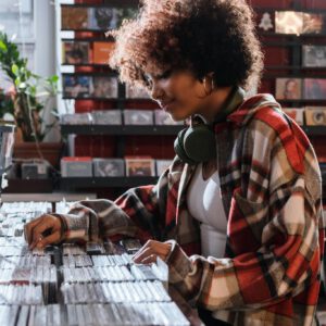 Curly-haired woman in a plaid shirt exploring compact discs at a music store.