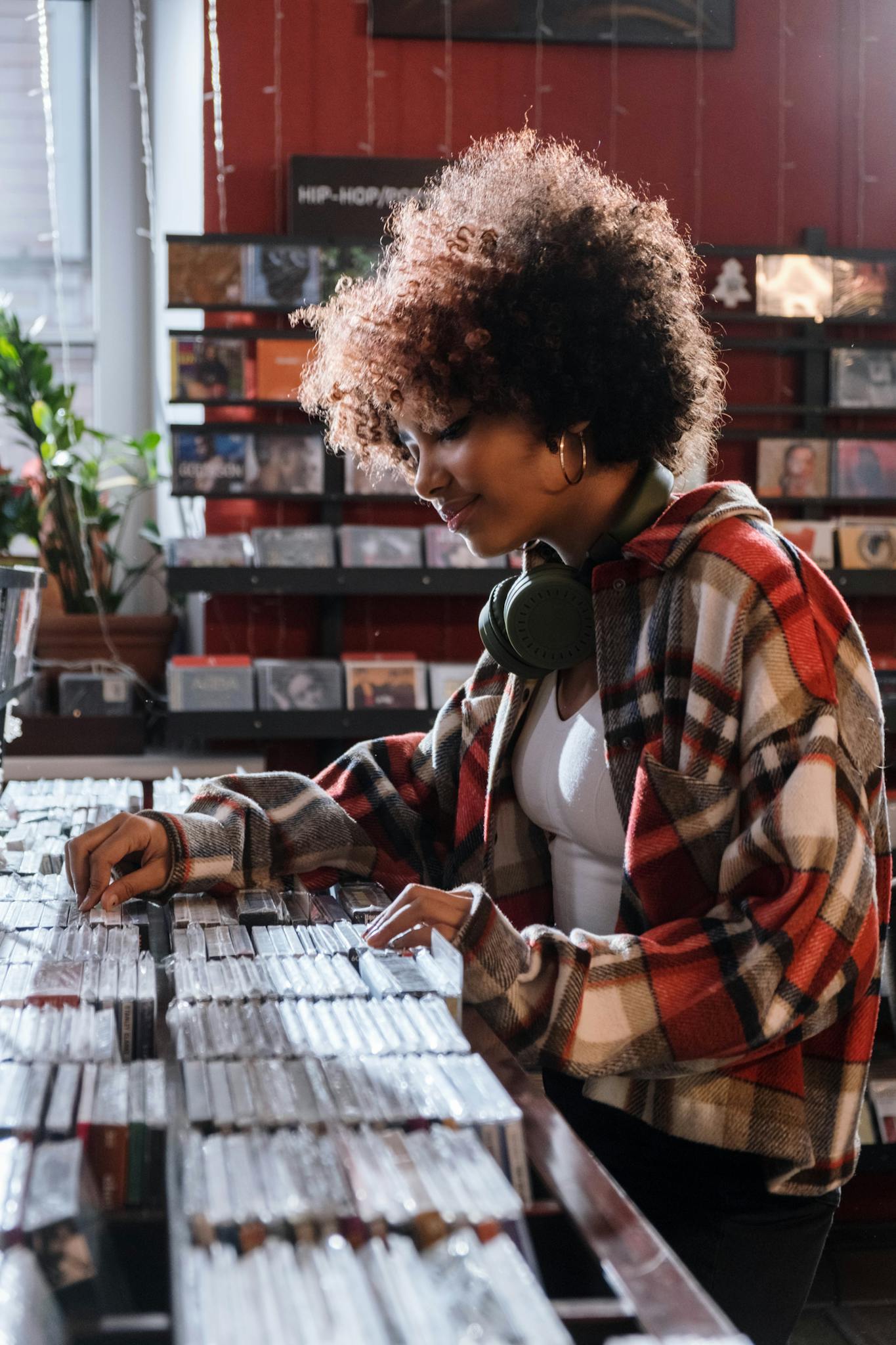 Curly-haired woman in a plaid shirt exploring compact discs at a music store.